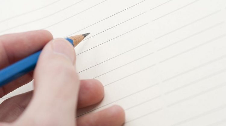 Hand holding pencil ready to write your message or text on a blank lined sheet of paper